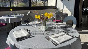 Una mesa de comedor redonda con mantel blanco, puesta con cubiertos, vasos y un florero con flores amarillas.