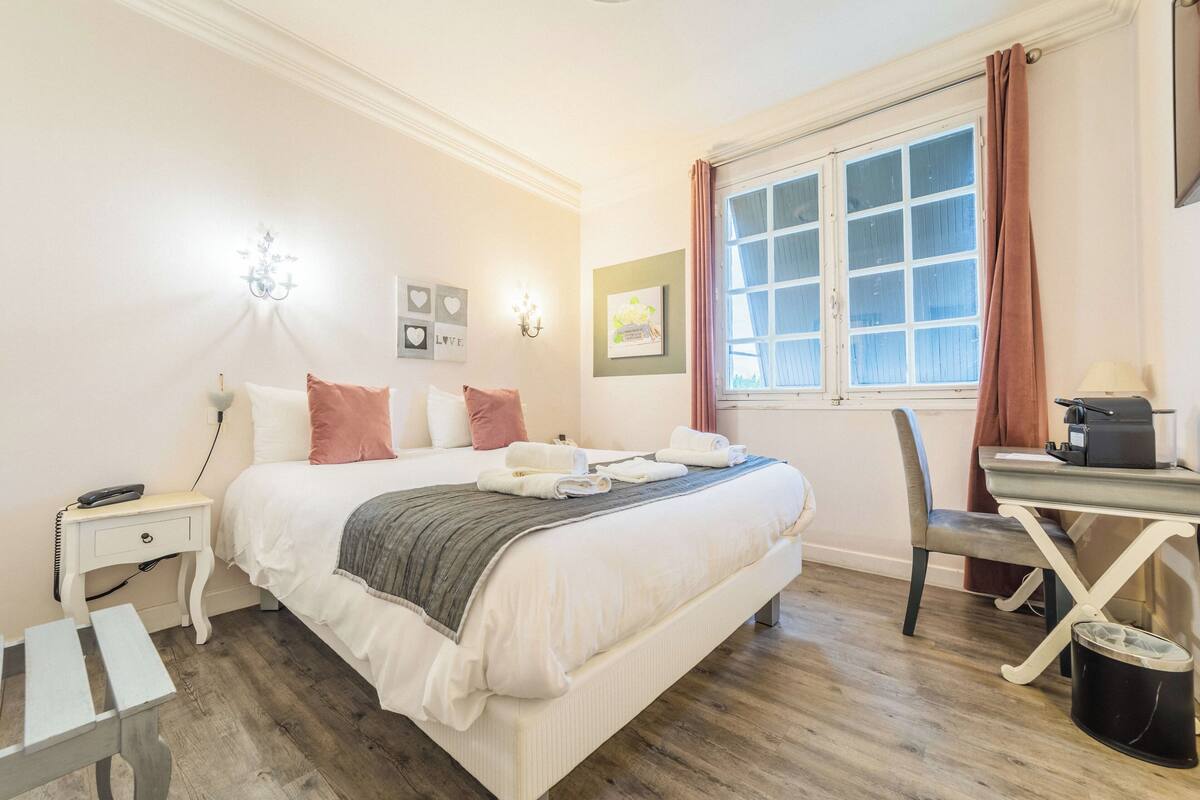 A neatly arranged bedroom with a bed, bedside table, lamp, and a desk with a chair.
