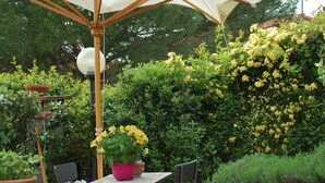 An outdoor patio with a table and chairs under a canopy, surrounded by potted plants and flowering bushes. - A wonderful country house in the heart of Chianti (Panzano In Chianti)
