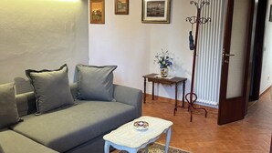 A living room with a grey sofa, a small white table, a patterned rug, a hanging light fixture, and a door leading to another room. - A wonderful country house in the heart of Chianti (Panzano In Chianti)