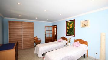 Two single beds with wooden headboards and white bedspreads, a large wardrobe, and a small table with a wicker basket.