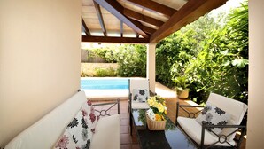 Un patio coperto con piscina, arredi da esterno e vegetazione lussureggiante.