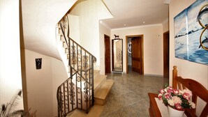 Una scala con ringhiera decorativa, un corridoio con pavimento piastrellato e un quadro appeso al muro.