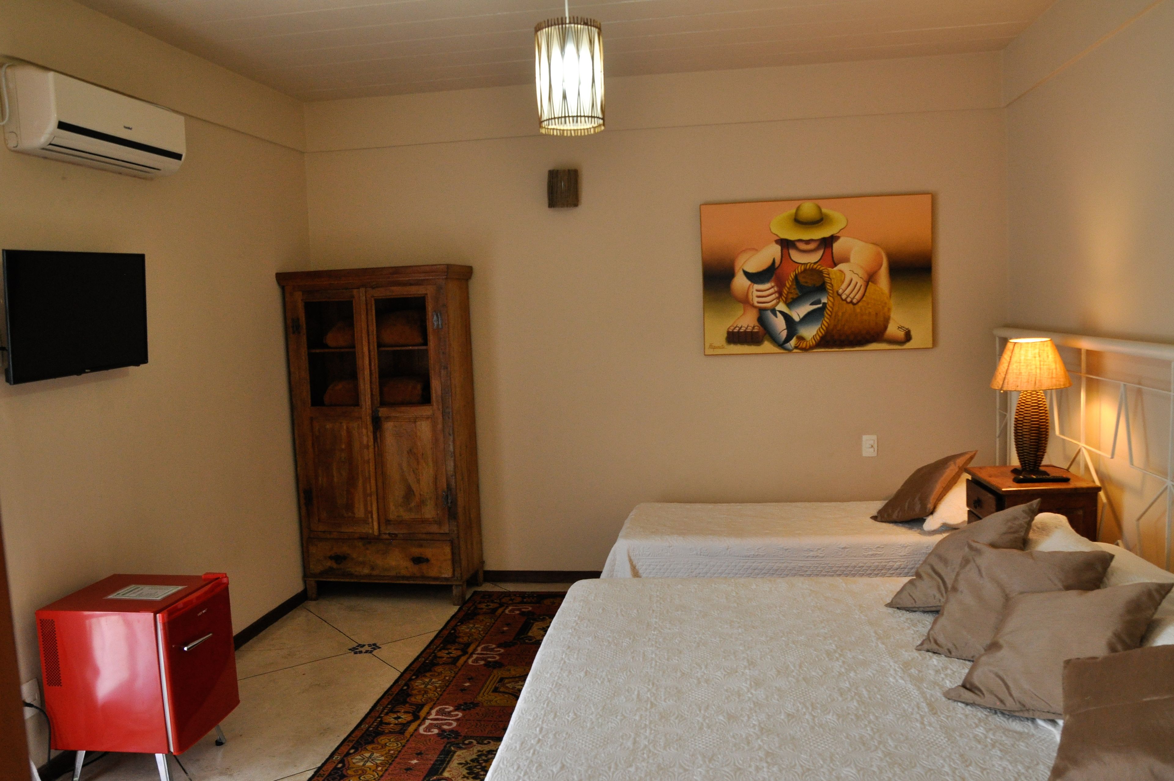 A room with two beds, a wooden cabinet, a red cabinet, a painting on the wall, and a lamp on a bedside table.