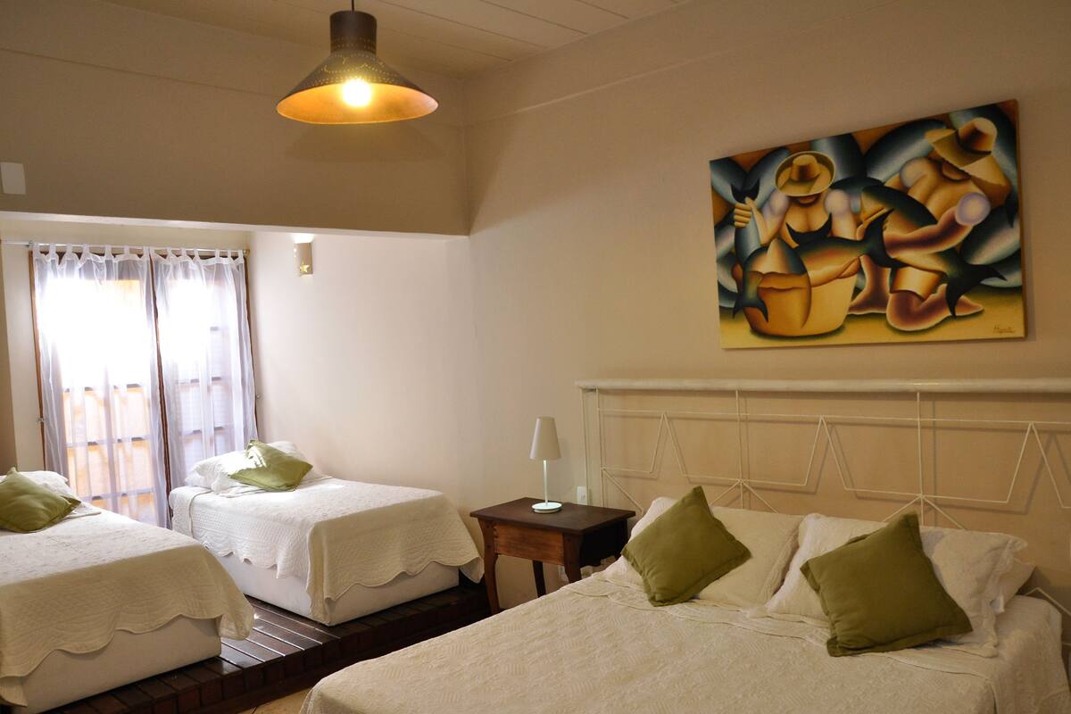 A hotel room with two beds, a nightstand, a painting, and a window with curtains.