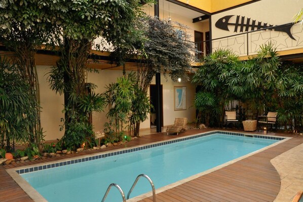Una piscina interior con cubierta de madera, rodeada de exuberante vegetación y un mural decorativo de peces.