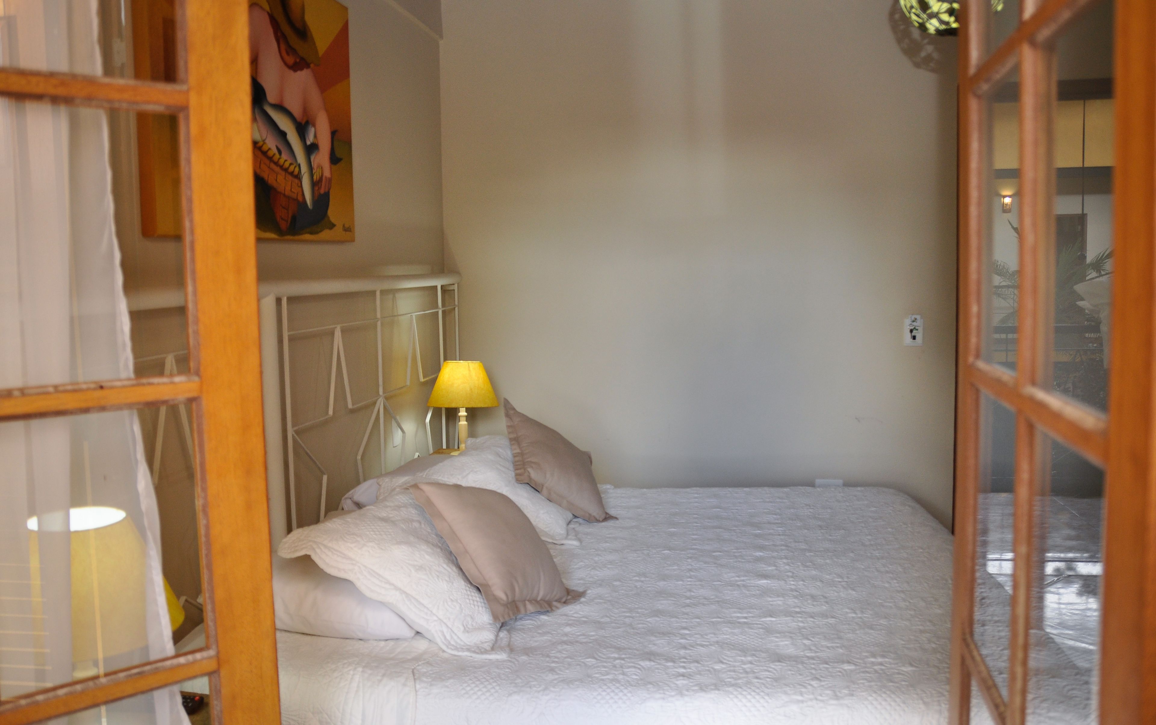 A neatly made bed with white and beige bedding, a bedside lamp, and a framed artwork on the wall.