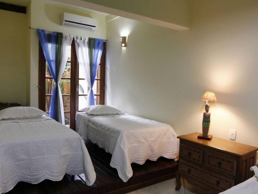 Un dormitorio con dos camas individuales, un aparador de madera, una mesita de noche con lámpara y un equipo de aire acondicionado.