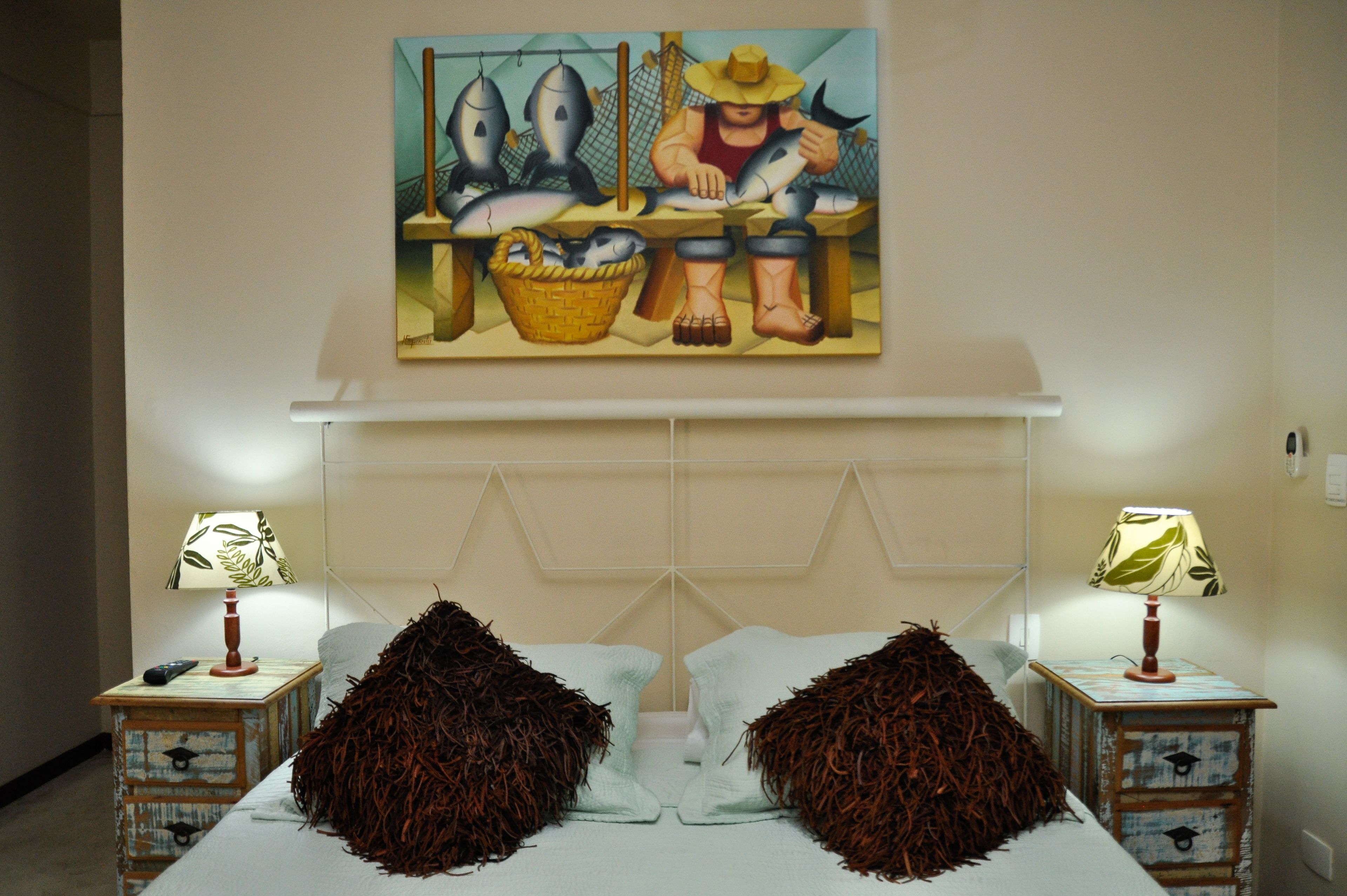 A bedroom with a bed, two nightstands with lamps, a painting above the bed, and a headboard.