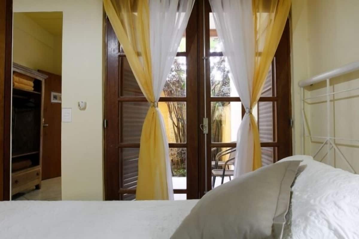 A bedroom with a bed, curtains, and a window with a view of the outdoors.