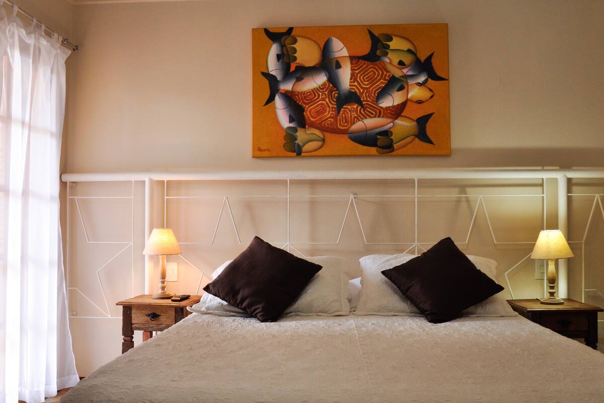 A neatly made bed with two pillows, two bedside tables with lamps, and a wall painting above the bed.