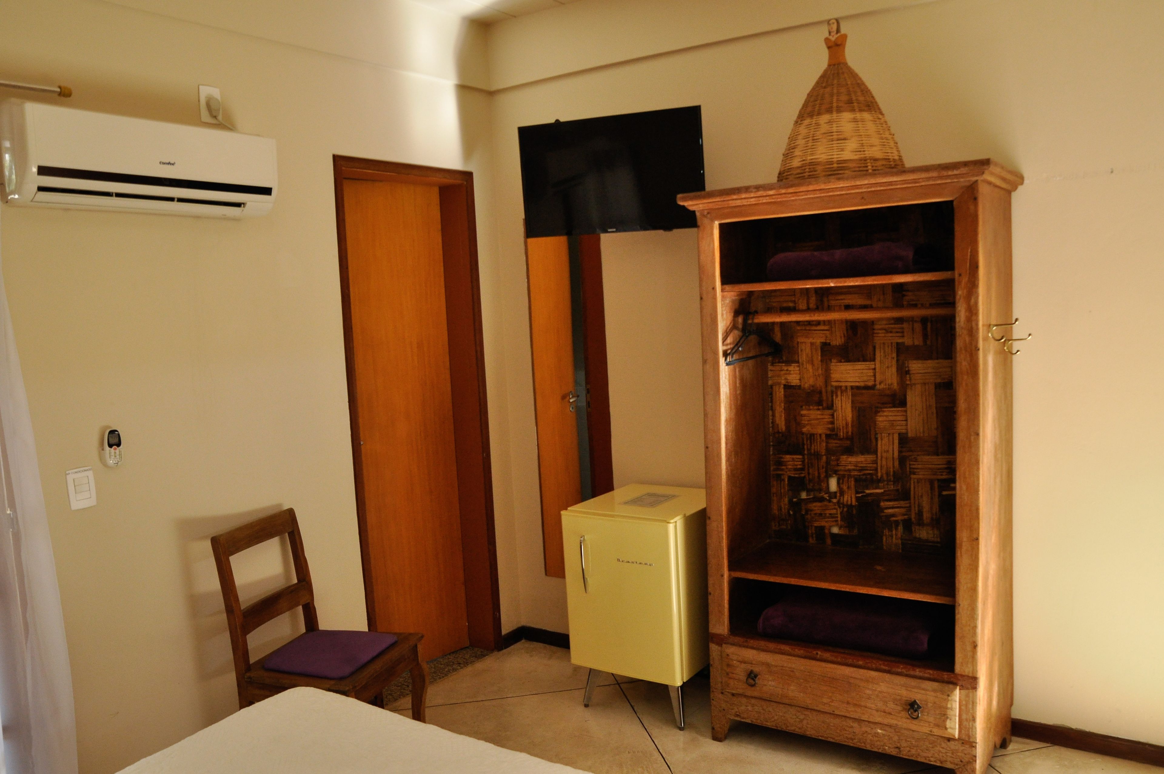 A compact room with a bed, a small wooden chair, a vintage-style wardrobe, and a wall-mounted air conditioner.