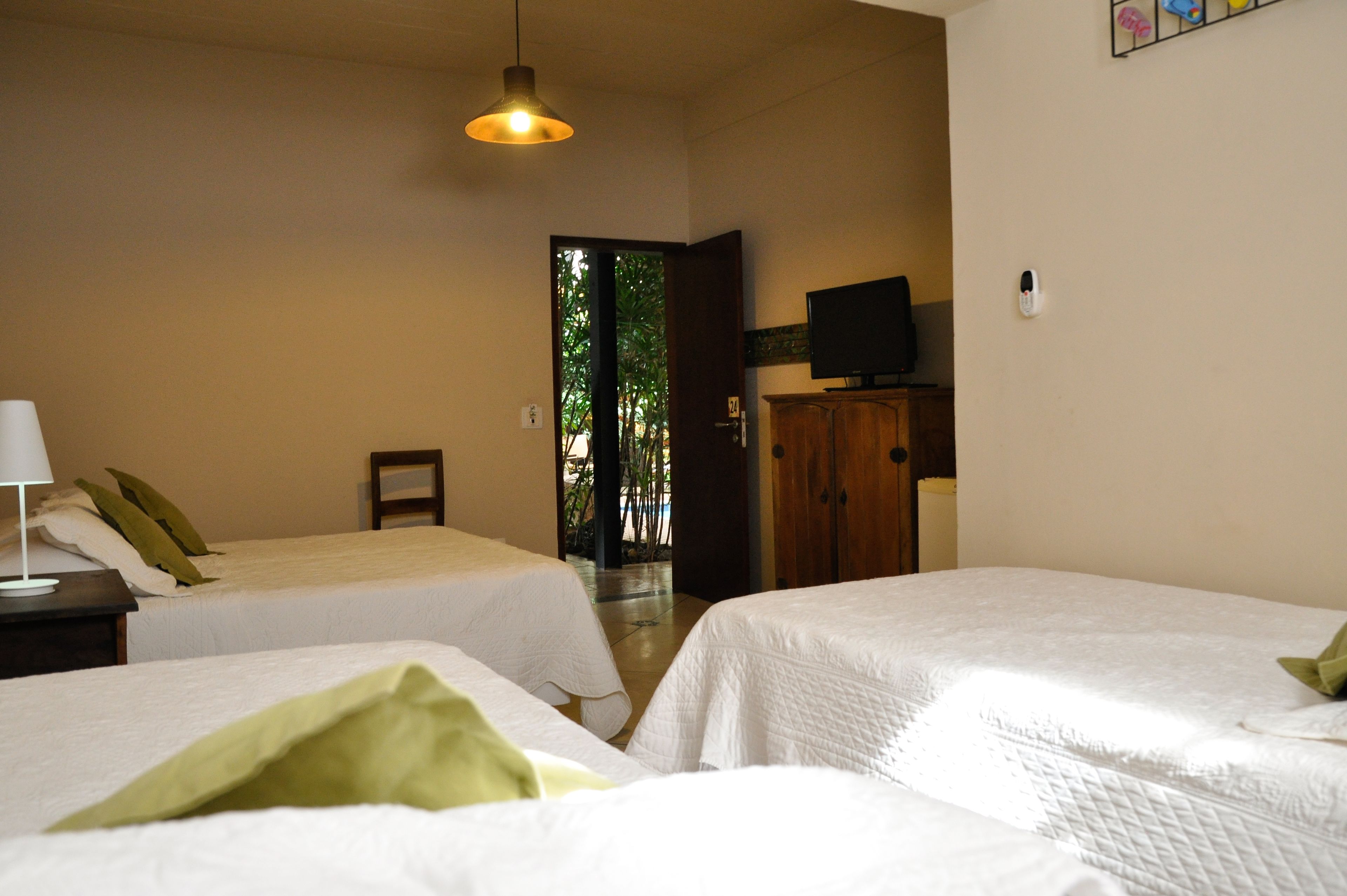 A hotel room with two single beds, a desk with a lamp, a television on the wall, and a view of greenery outside.