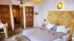 A bedroom with a large bed, a wooden headboard, a bedside table, a bench, and a hanging light fixture. - Dar Chadia (Marrakech)