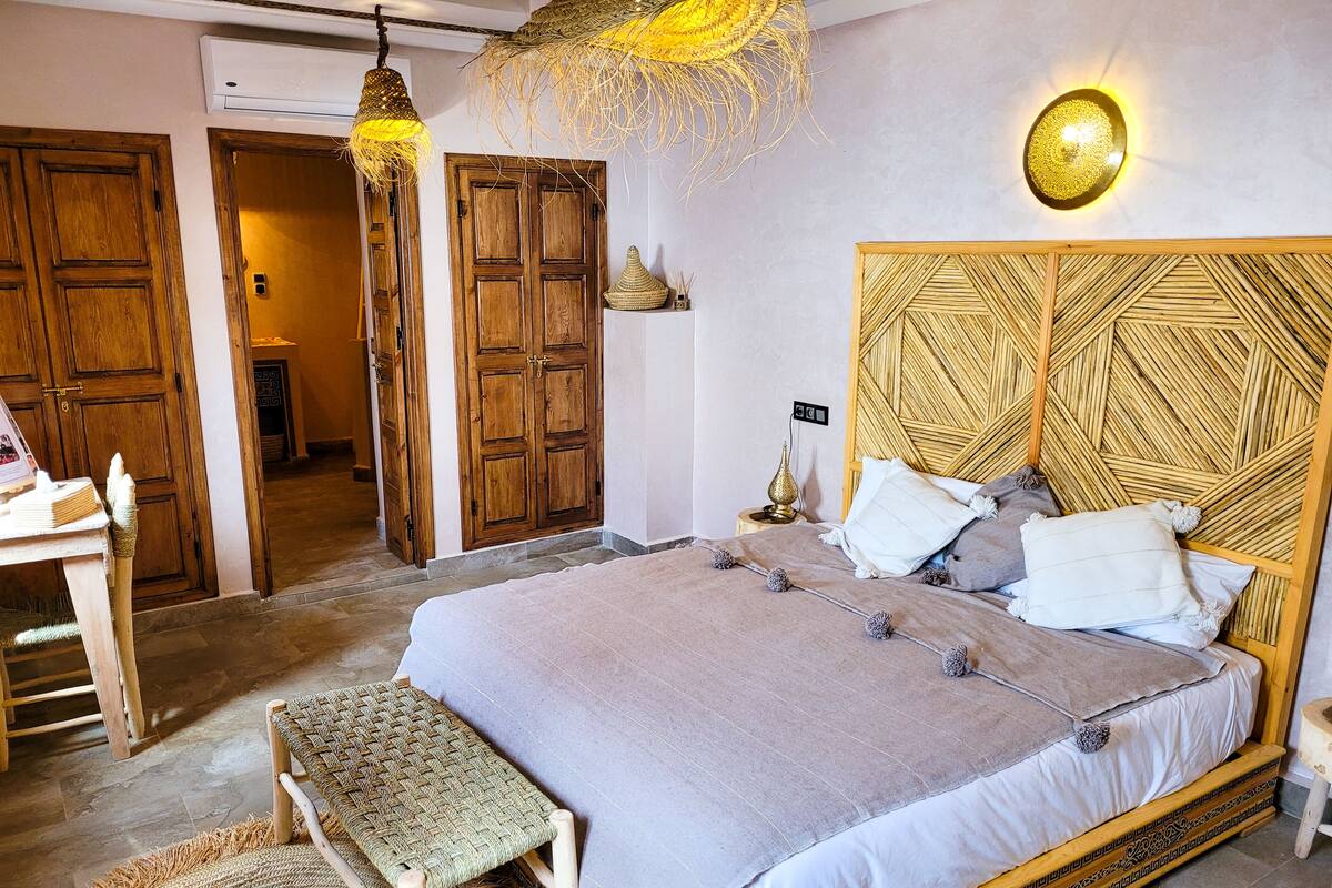 A bedroom with a large bed, a wooden headboard, a bedside table, a bench, and a hanging light fixture.