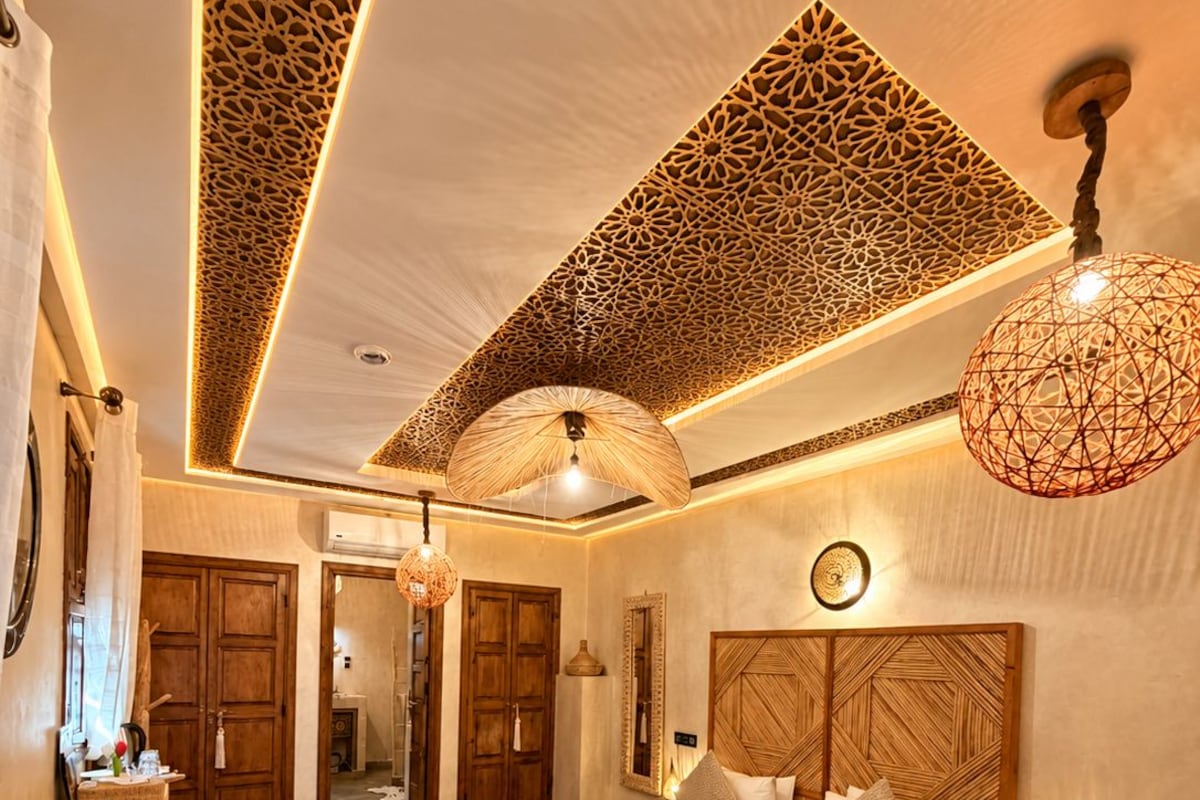 A spacious bedroom with a large bed, a wooden headboard, a round rug, and a hanging light fixture.