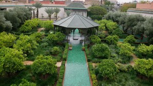 A lush garden with a central water feature, a gazebo, and a view of surrounding buildings. - Dar Chadia (Marrakech)