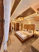 Un dormitorio amplio con una cama grande, cabecera de madera, alfombra redonda y un techo decorativo.