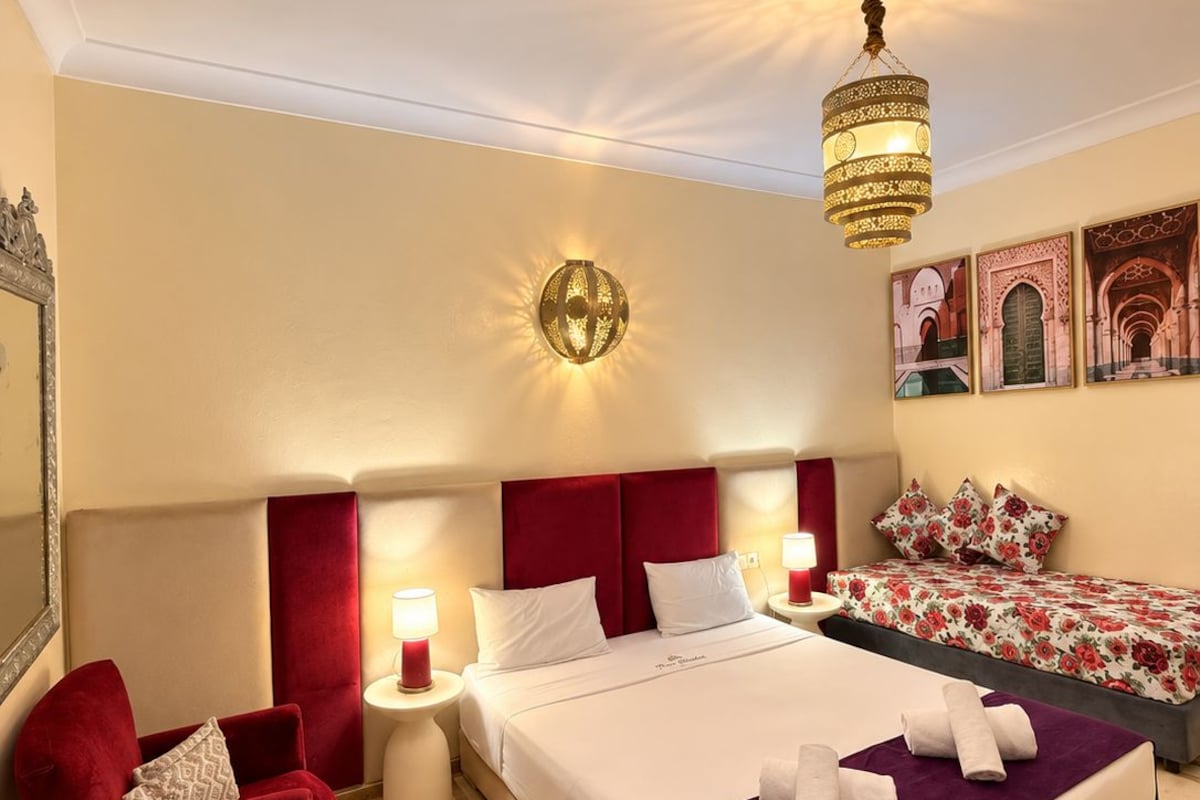 A hotel room with a large bed, a red armchair, a small table with a lamp, and a decorative ceiling light.