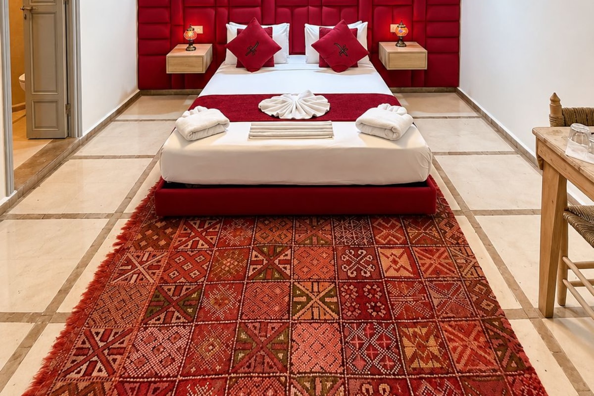 A hotel room with a large bed, a red headboard, a patterned rug, and a unique ceiling light fixture.