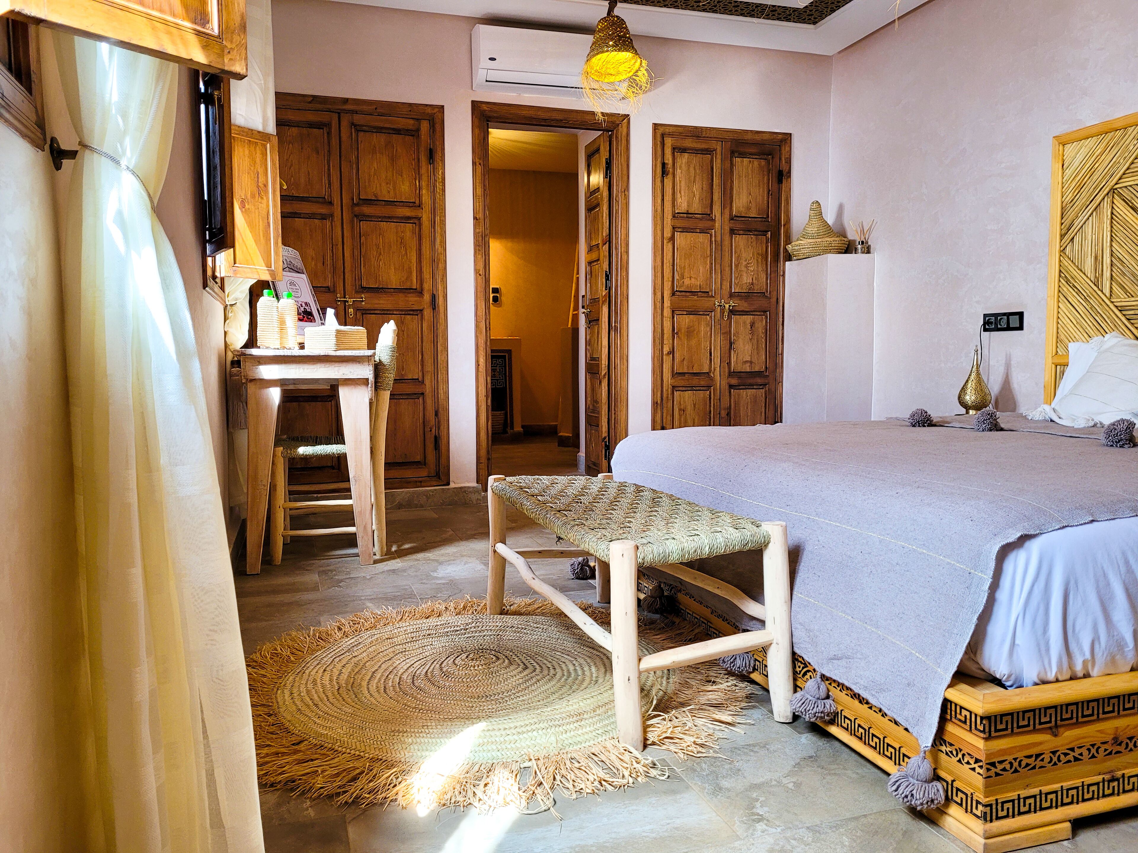 Una stanza con un letto, una panca in legno, una scrivania e un tappeto intrecciato.