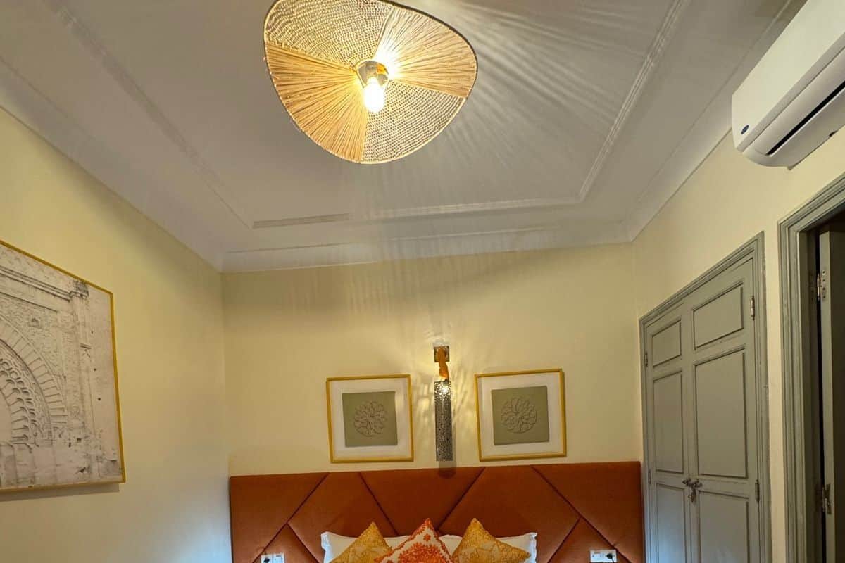 A hotel room with a bed, a ceiling fan, framed artwork on the wall, and a door.