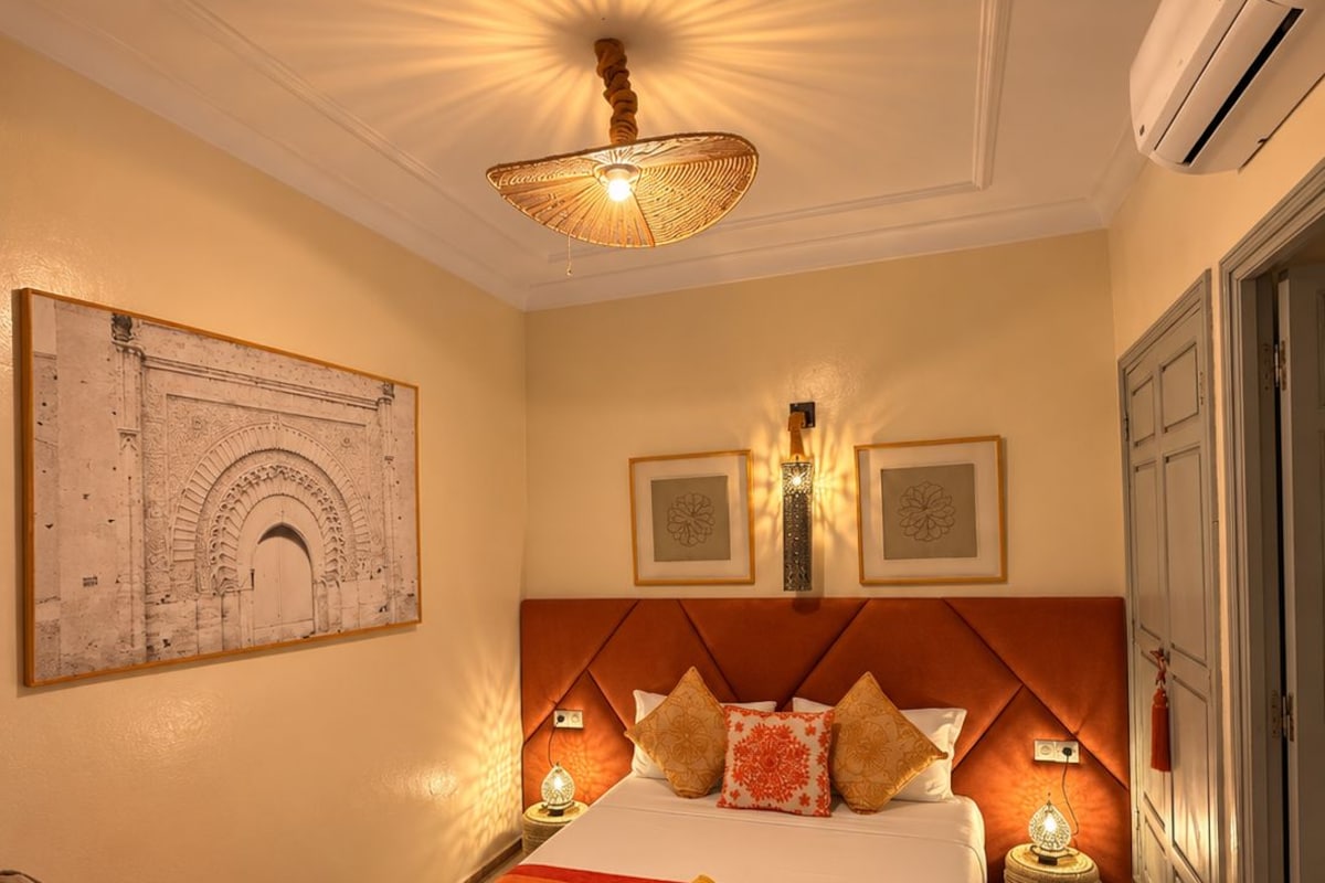 A hotel room with a large bed, a wall-mounted artwork, a ceiling light fixture, and a wall-mounted air conditioning unit.