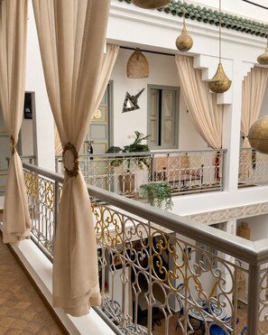 Un balcón con barandillas de metal decorativas, cortinas color beige y lámparas colgantes.