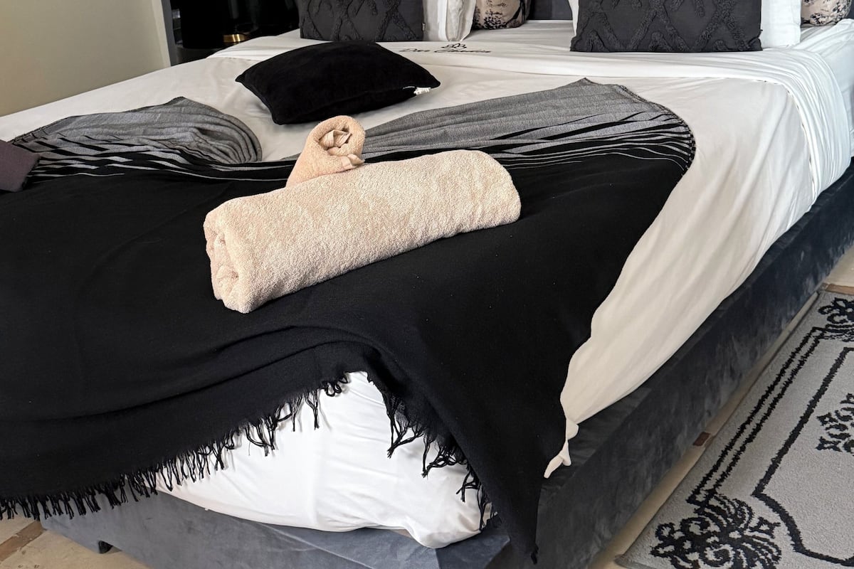 A neatly made bed with a patterned bedspread, a rolled towel, and a decorative wall plate above it.