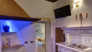 Un couloir bien éclairé, avec une étagère illuminée de lumière bleue, un téléviseur fixé au mur et un chandelier décoratif.