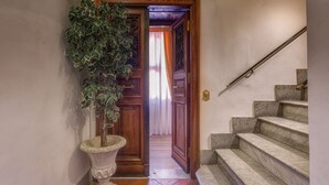 Un couloir avec une porte en bois donnant sur une pièce, une plante en pot et un escalier en marbre.