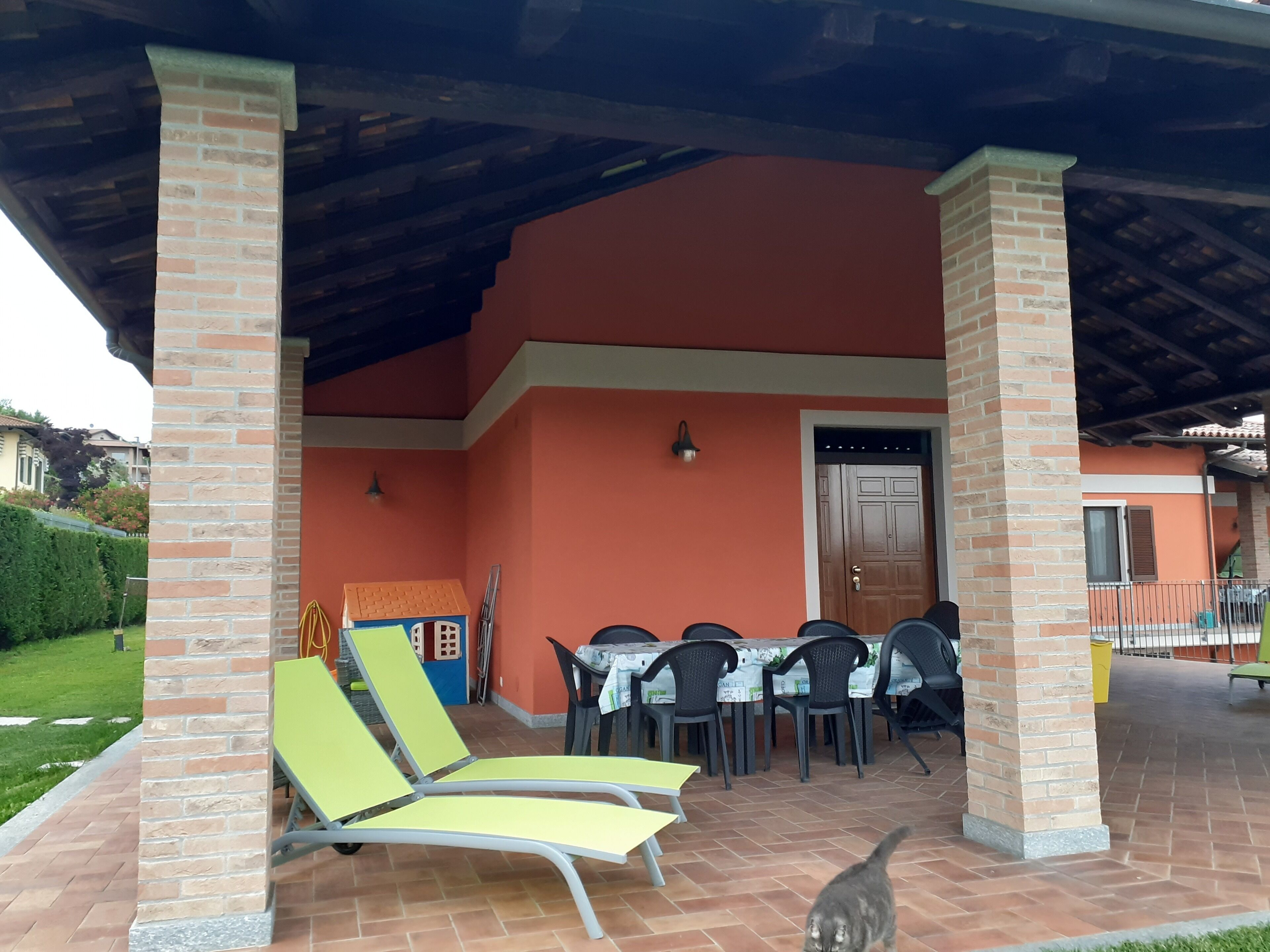 Un’area salotto all'aperto coperta, con pilastri in mattoni, un tavolo e sedie, e una porta.