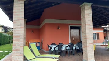 Un’area salotto all'aperto coperta, con pilastri in mattoni, un tavolo e sedie, e una porta.