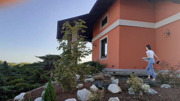 Une maison moderne à l’extérieur rouge, avec un chemin de pierre et un jardin agrémenté de diverses plantes et roches.