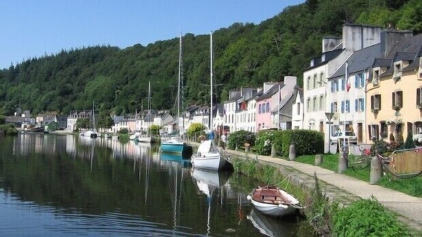 A calm waterfront with boats docked along the shore, surrounded by colorful buildings and lush greenery.