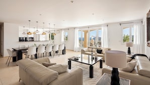 A spacious living area with a sofa, coffee table, and dining set. There is a kitchen area with modern appliances and pendant lighting. Large windows offer a view of the outdoors. - Villa 55 -Heated pool with exceptional view (Roquebrune-Sur-Argens)