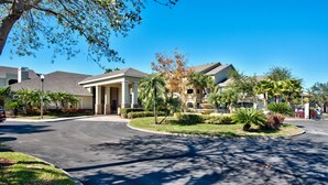 A residential area with a curved driveway leading to a gated entrance, surrounded by well-maintained lawns and palm trees. - Avalon Ground floor condo (clearwater)