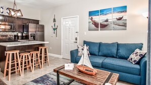 A modern kitchen with stainless steel appliances, a blue sofa, and a coffee table with a model sailboat. - Avalon Ground floor condo (clearwater)