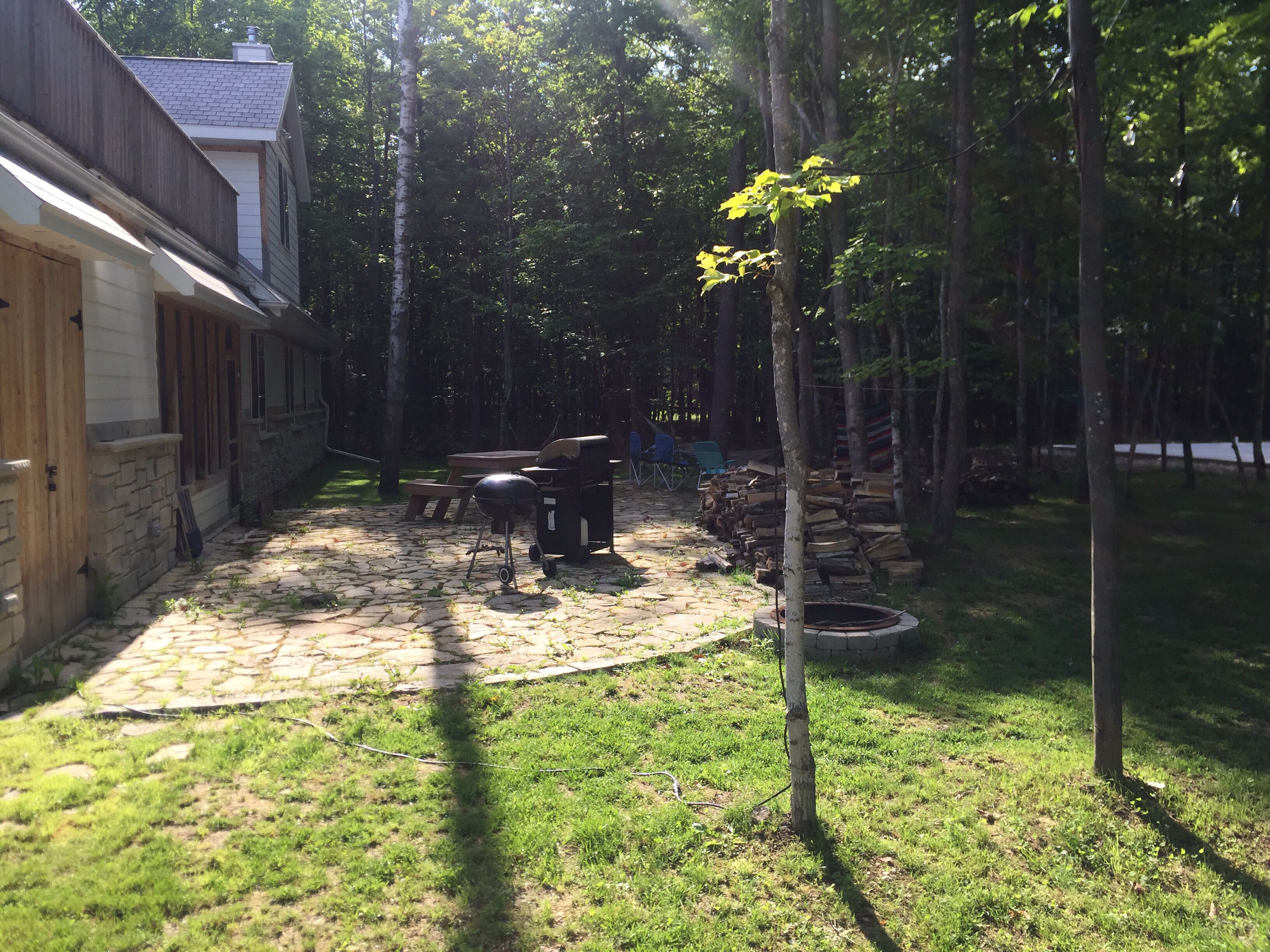 Un jardin avec une terrasse en pierre, un barbecue et une terrasse en bois.