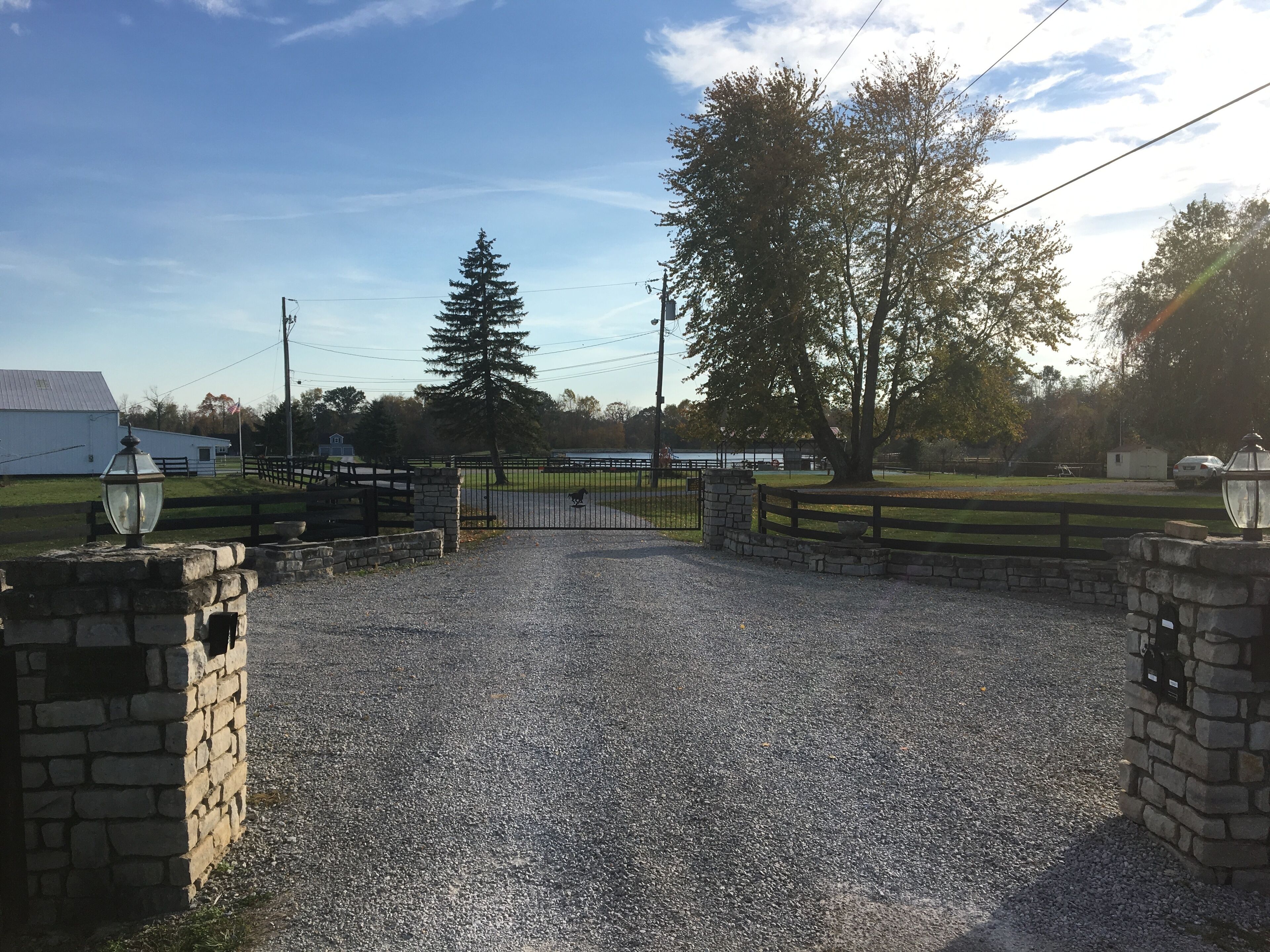 A gravel driveway leading to a gated entrance with stone walls and a metal gate.