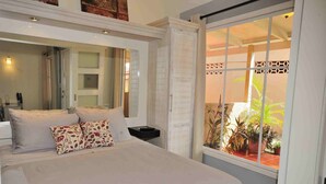 Un dormitorio con una cama grande, una mesita de noche, un espejo y vistas a un balcón con plantas.