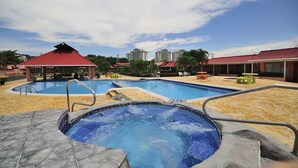 Un área de piscina con jacuzzi, sillas de descanso y un pabellón.
