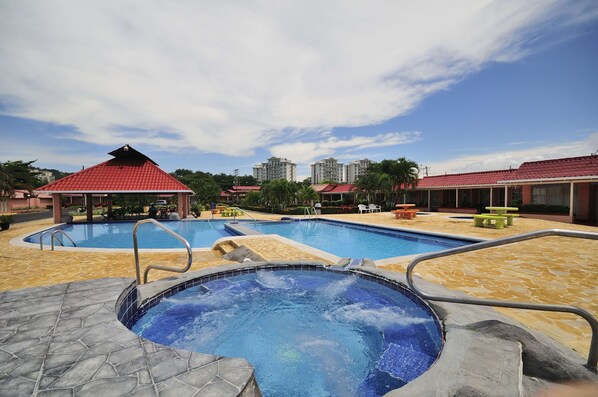 Un área de piscina con jacuzzi, sillas de descanso y un pabellón.