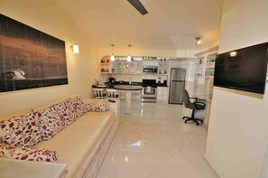 A modern living room with a sofa, a dining table, and a kitchen area with a TV.