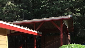 A covered wooden structure with a red roof, a gravel pathway, and a small garden with flowers and shrubs.