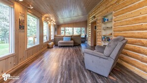 A log cabin interior with a wooden floor, a sofa, a chair, and a bookshelf.