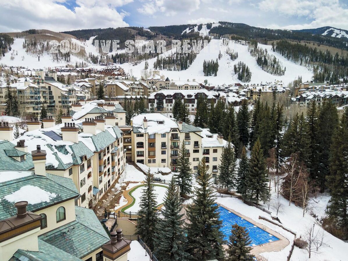 A resort with multiple buildings, a swimming pool, and a snowy mountain backdrop.