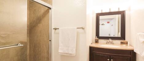 A bathroom with a shower, a sink, a mirror, and a towel rack.