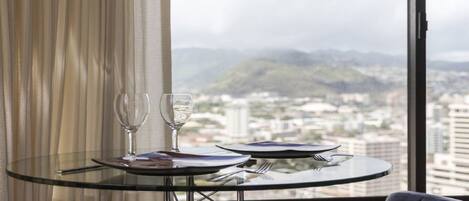 A dining table with two wine glasses and cutlery, set against a window with a cityscape and mountains in the background.