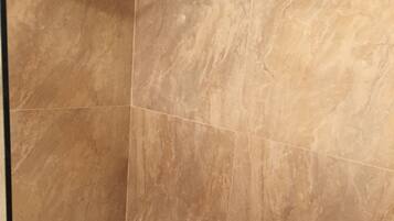 A shower area with a handheld showerhead and a wall-mounted control.